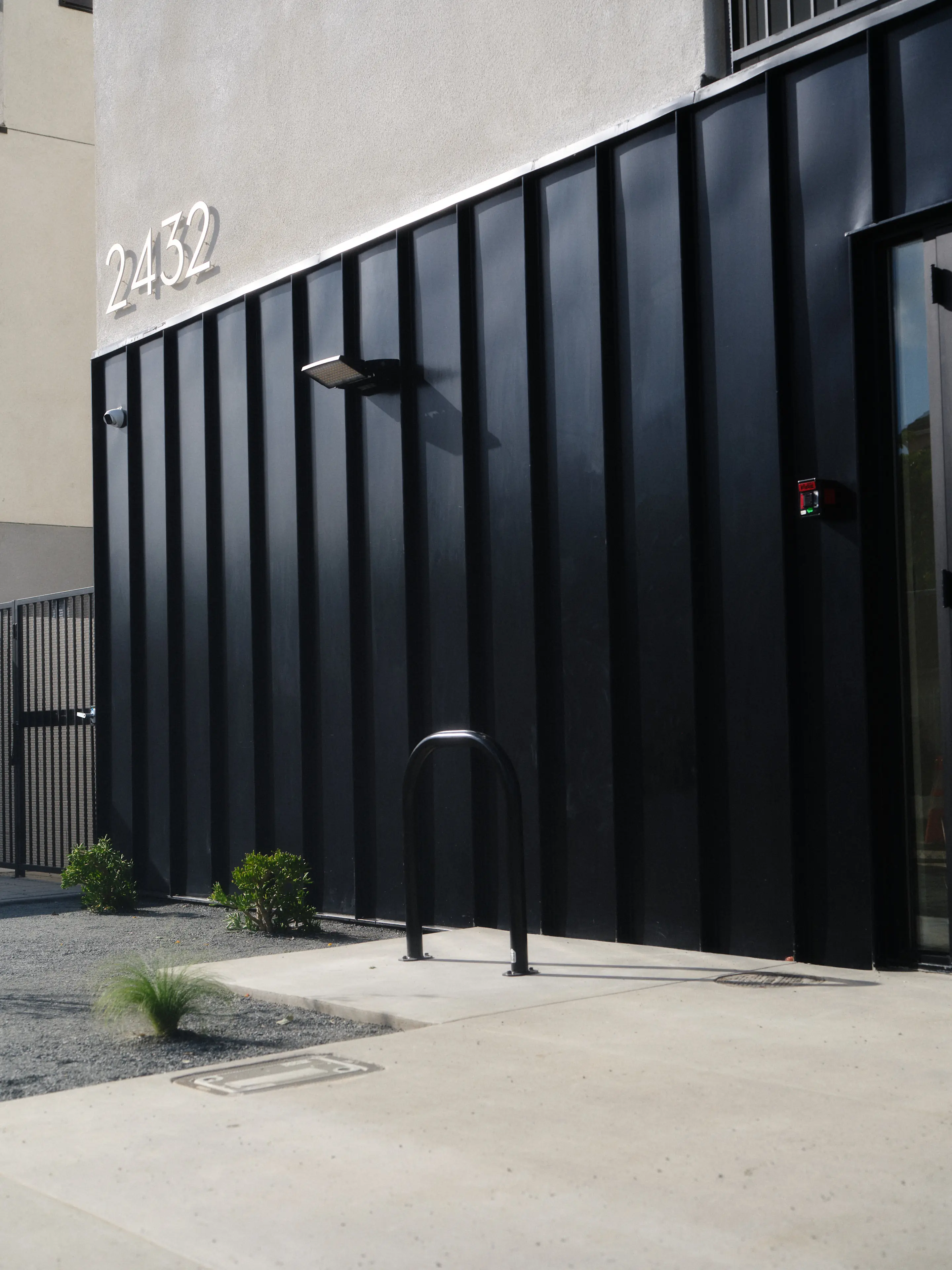 Modern building with black vertical panels, number 2432 on beige wall, and a bike rack on concrete.