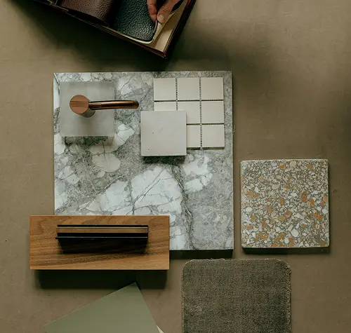 Flat lay of marble, tile, wood samples, fabric swatch, and hardware on neutral surface.