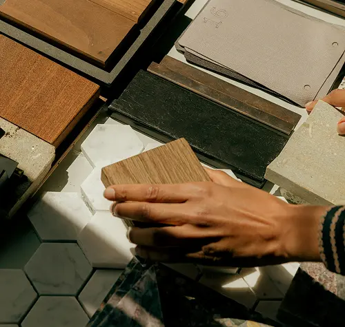 Two hands holding wood and stone tile samples over a variety of tile and wood materials.